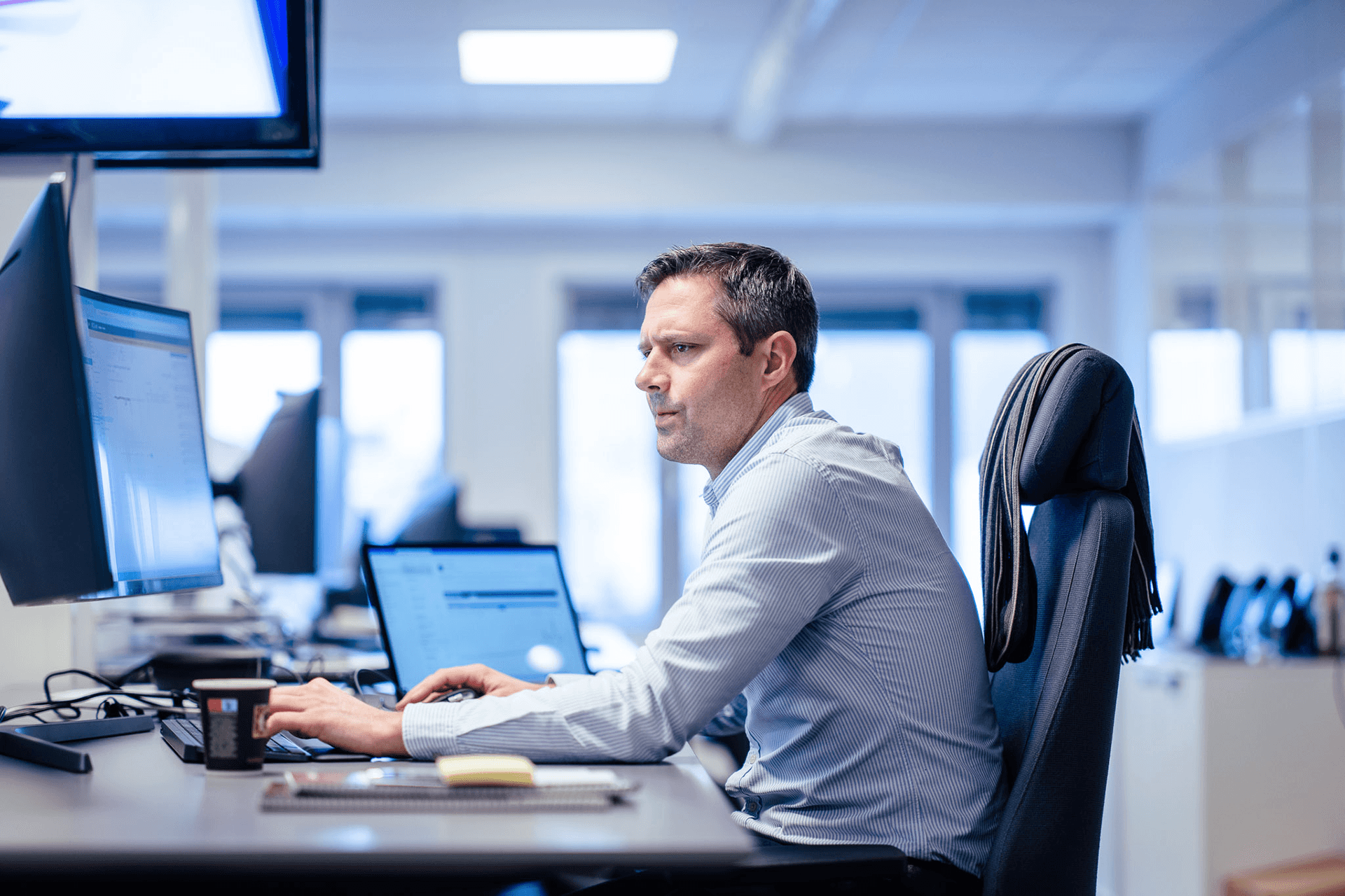 Image of a man Man sitting in front of three screens to illustrate production planning and trading