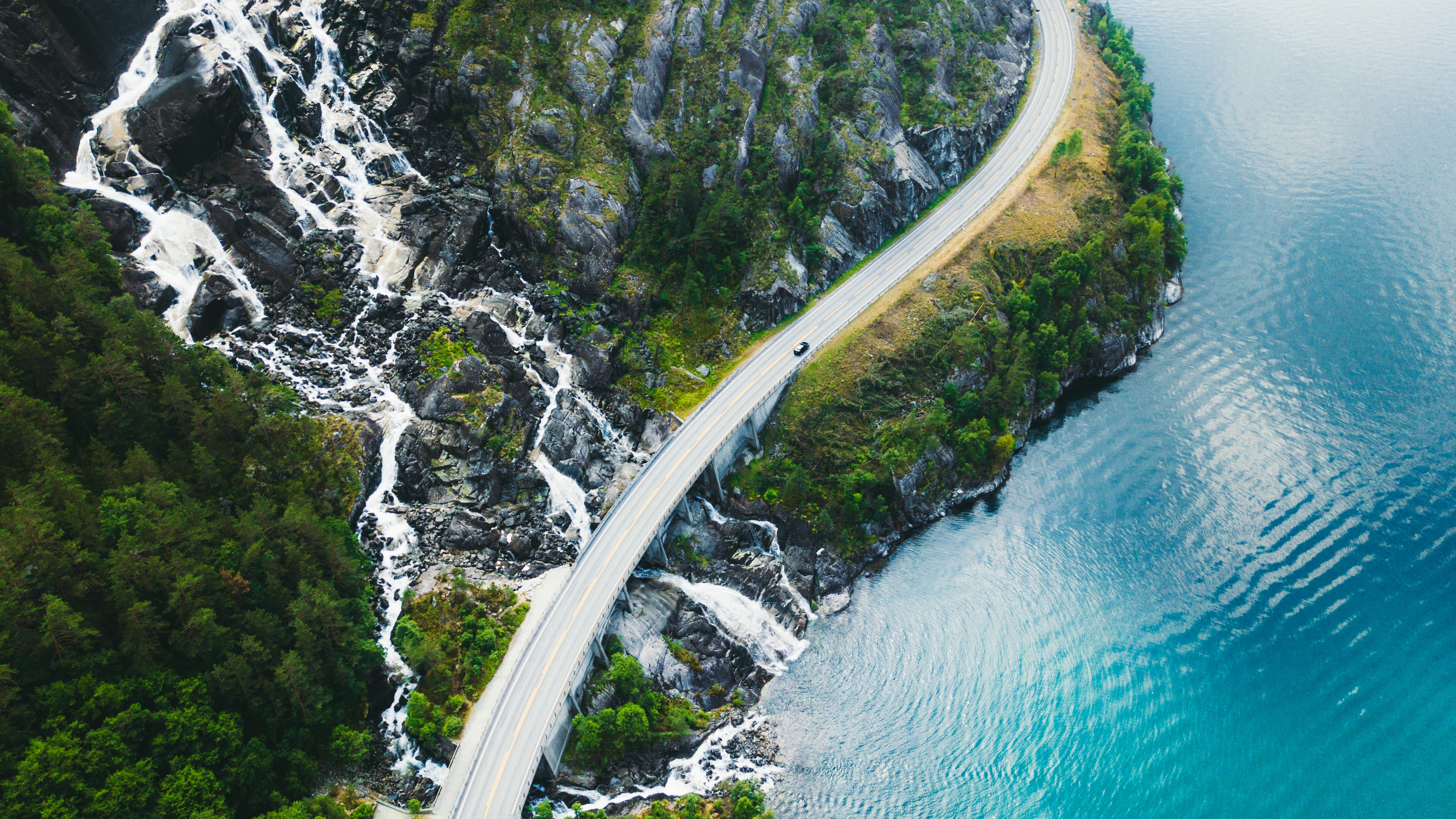 Highway with waterfall on the left side and car driving on the road in the middel with ocean on the right side.